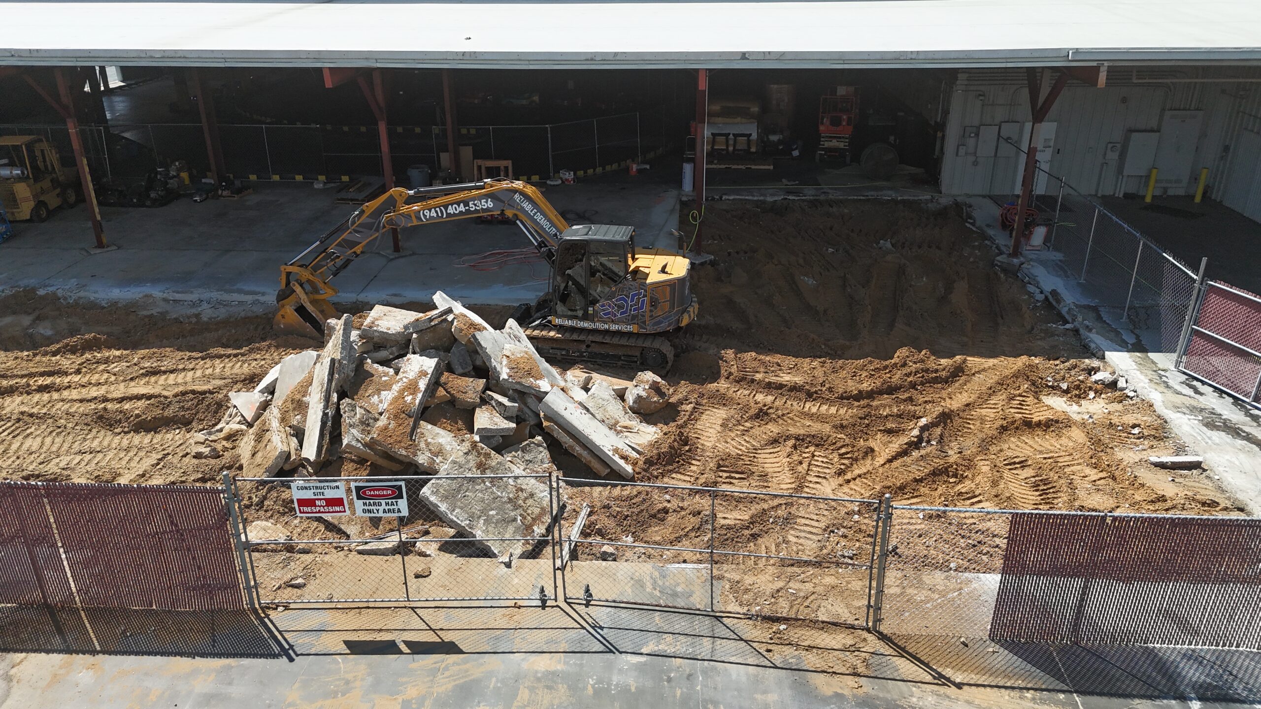 default Reliable Demolition Services excavator tearing down a house with a roll-off dumpster on site